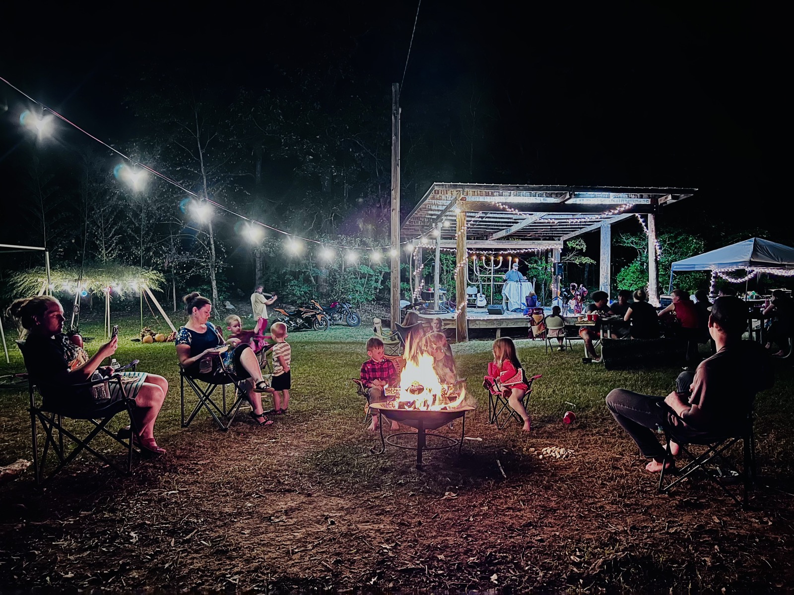 Family gathered around a campfire with string lights at the Feast